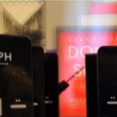 Czarne urządzenia audioprzewodników  na tle plakatu wystawy Dom ze snów